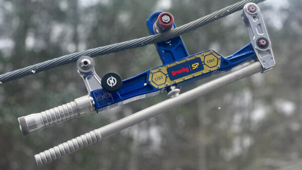 Cable tension meter with blue and silver design on wire against blurred outdoor background.