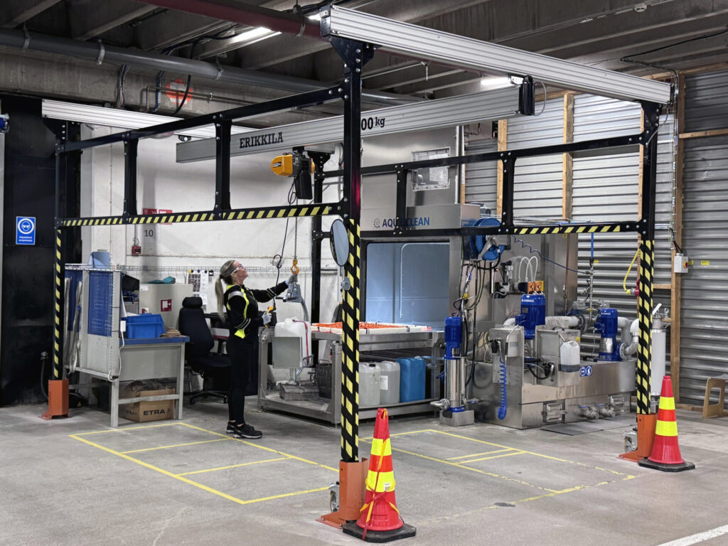 Worker operating industrial equipment in a factory with safety gear and caution indicators.